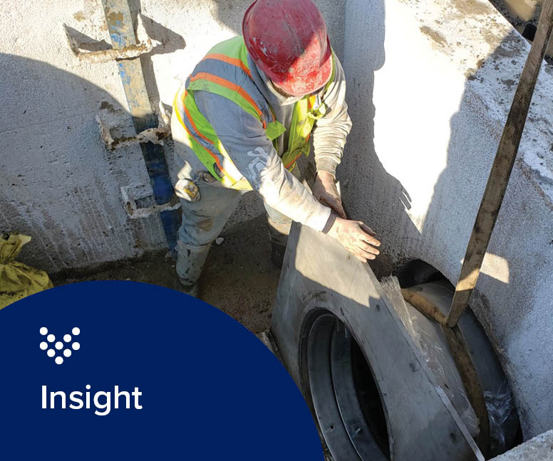 A construction worker in a hard hat installing a check valve on a sewage system.