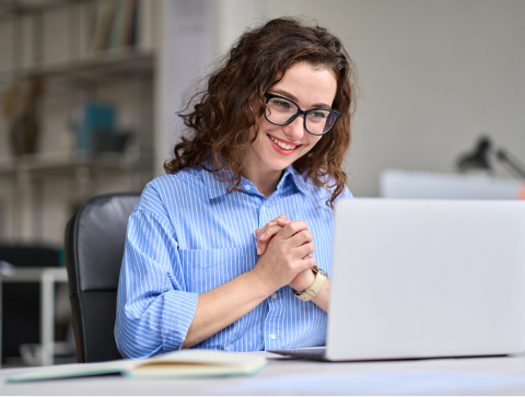A woman with glasses sitting at a computer smiling
